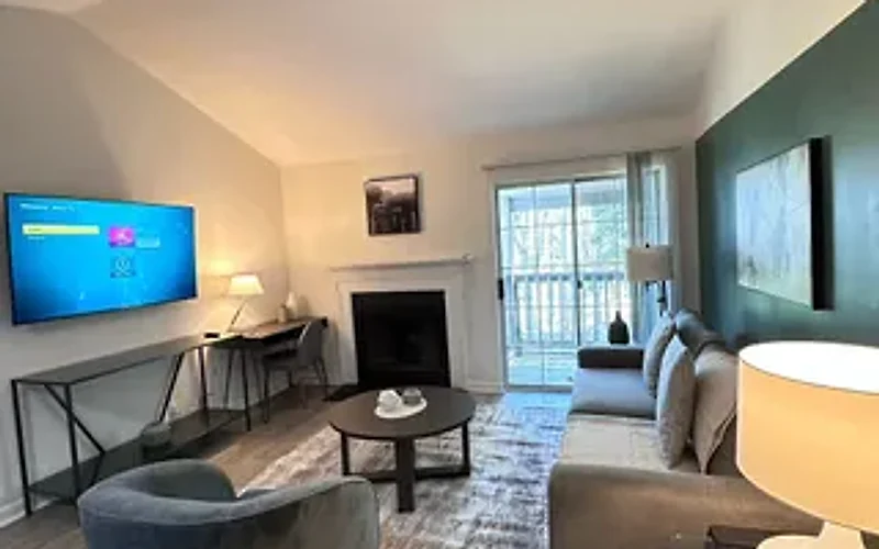 Furnished rental living room with a wall-mounted TV, a desk, lamps and a dark green accent wall