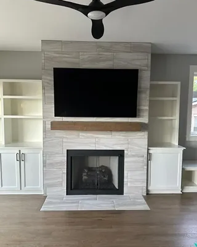 Flat-screen TV mounted on a tiled fireplace surround above a wood mantel, with white built-in shelves on both sides