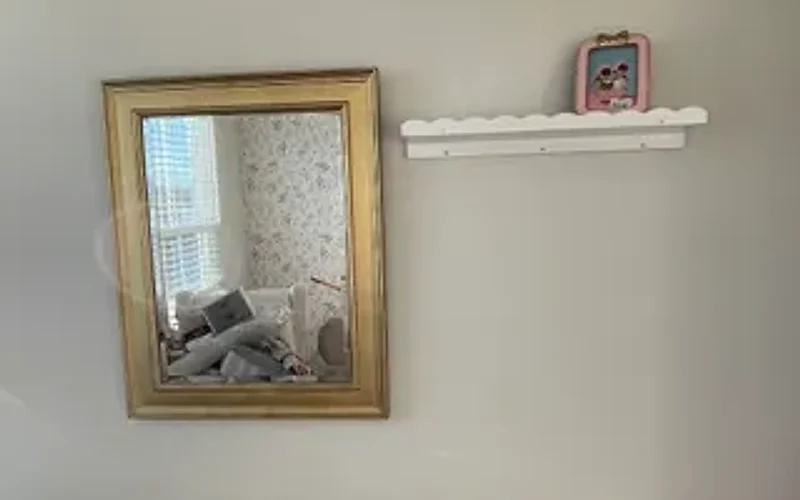 Framed mirror hung level on a bedroom wall next to a scalloped floating shelf, both mounted in the same visit